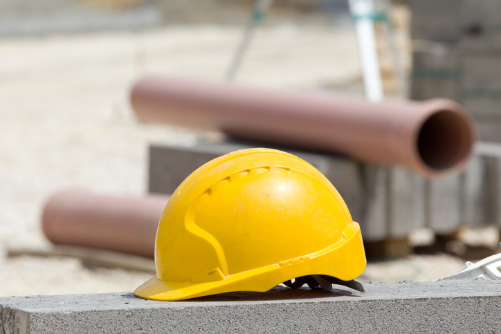 Yellow helmet standing on concrete roadside at construction site. Plastic pipes and roadside blocks in background